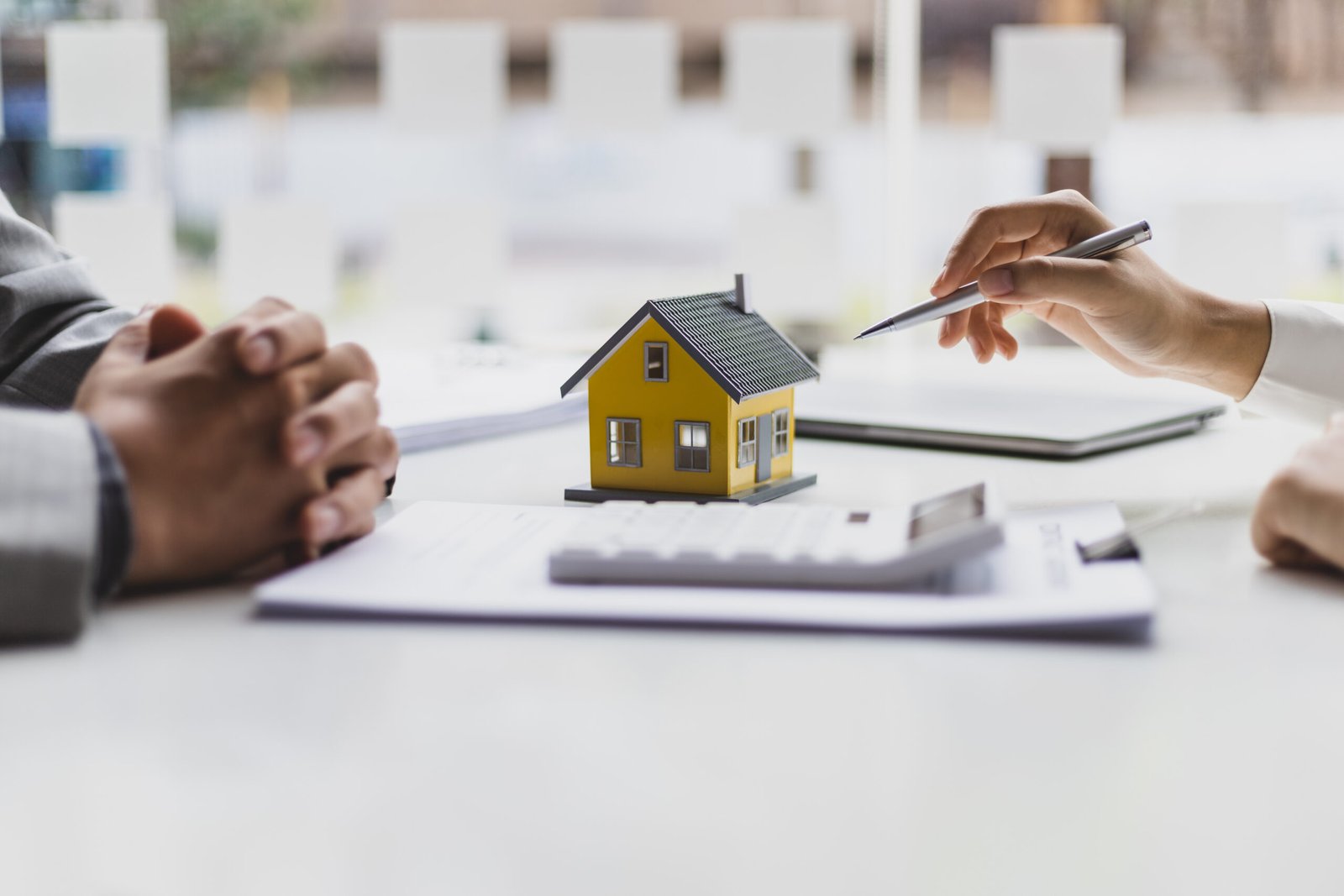 Dans un bureau d'agent immobilier, une maquette de maison attire l'attention au centre de la table alors qu'un acheteur potentiel se prépare à prendre des décisions importantes, guidé par un professionnel.