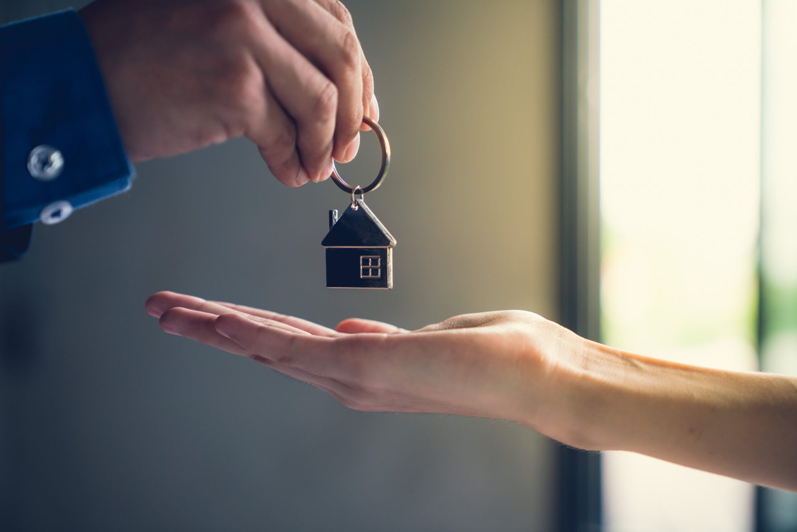 Le transfert d'une clé de maison symbolique d'une main à une autre dans un contexte lumineux et flou, suggérant une transaction immobilière réussie et l'excitation d'un nouveau départ.